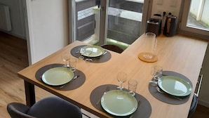 Ein moderner Essbereich mit einem Holztisch, gedeckt für vier Personen, mit schwarzen Tischsets und grünen Tellern.