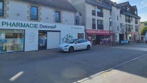 Straßenansicht mit einem weißen Auto, das vor einer Apotheke namens 'Delcroix' und einer orthopädischen Klinik geparkt ist.