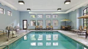 A swimming pool with clear water, surrounded by lounge chairs and a table with umbrellas. - Equipped Suite | Business Center + Indoor Pool (Kalamazoo)