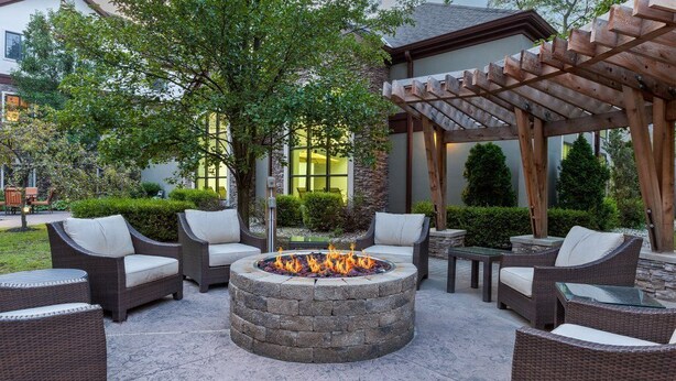 A patio area with wicker furniture, a stone fire pit, and a pergola structure. - Equipped Suite | Business Center + Indoor Pool (Kalamazoo)