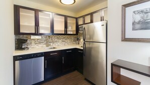 A compact kitchen with dark cabinets, a stainless steel refrigerator, a dishwasher, and a tiled backsplash.