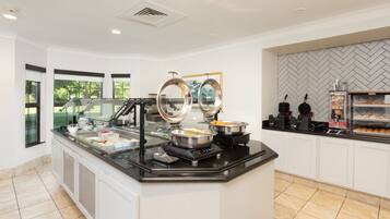 A buffet area with a glass counter, stainless steel bowls, and a coffee machine.