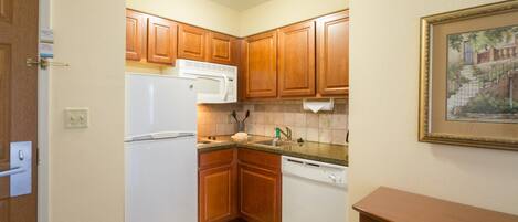 A compact kitchen with wooden cabinets, a white refrigerator, a microwave, and a dishwasher.