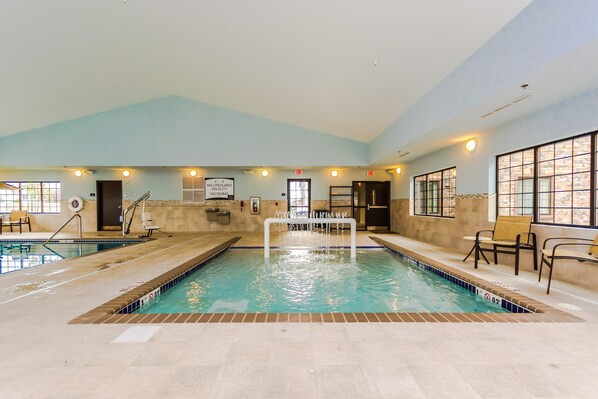 An indoor swimming pool with clear water, two exits, and a lifeguard sign.