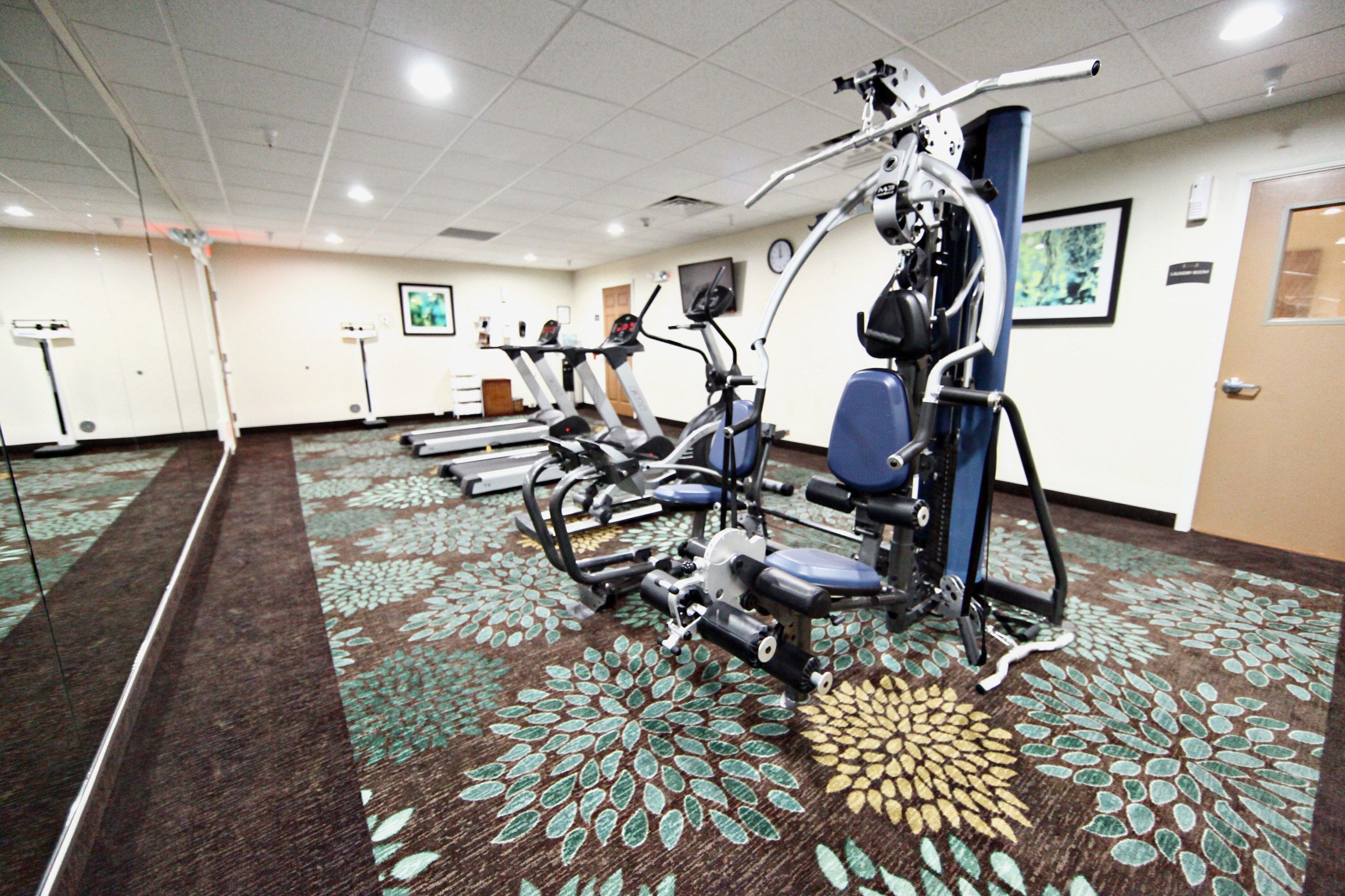 A gym with exercise equipment, carpeted floor, and a door.