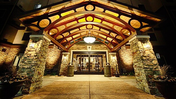 L’entrée d’un hôtel, avec une façade en pierre, une arche en bois et une grande porte vitrée.