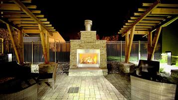 An outdoor patio with a stone fireplace, wicker furniture, and a pergola structure.