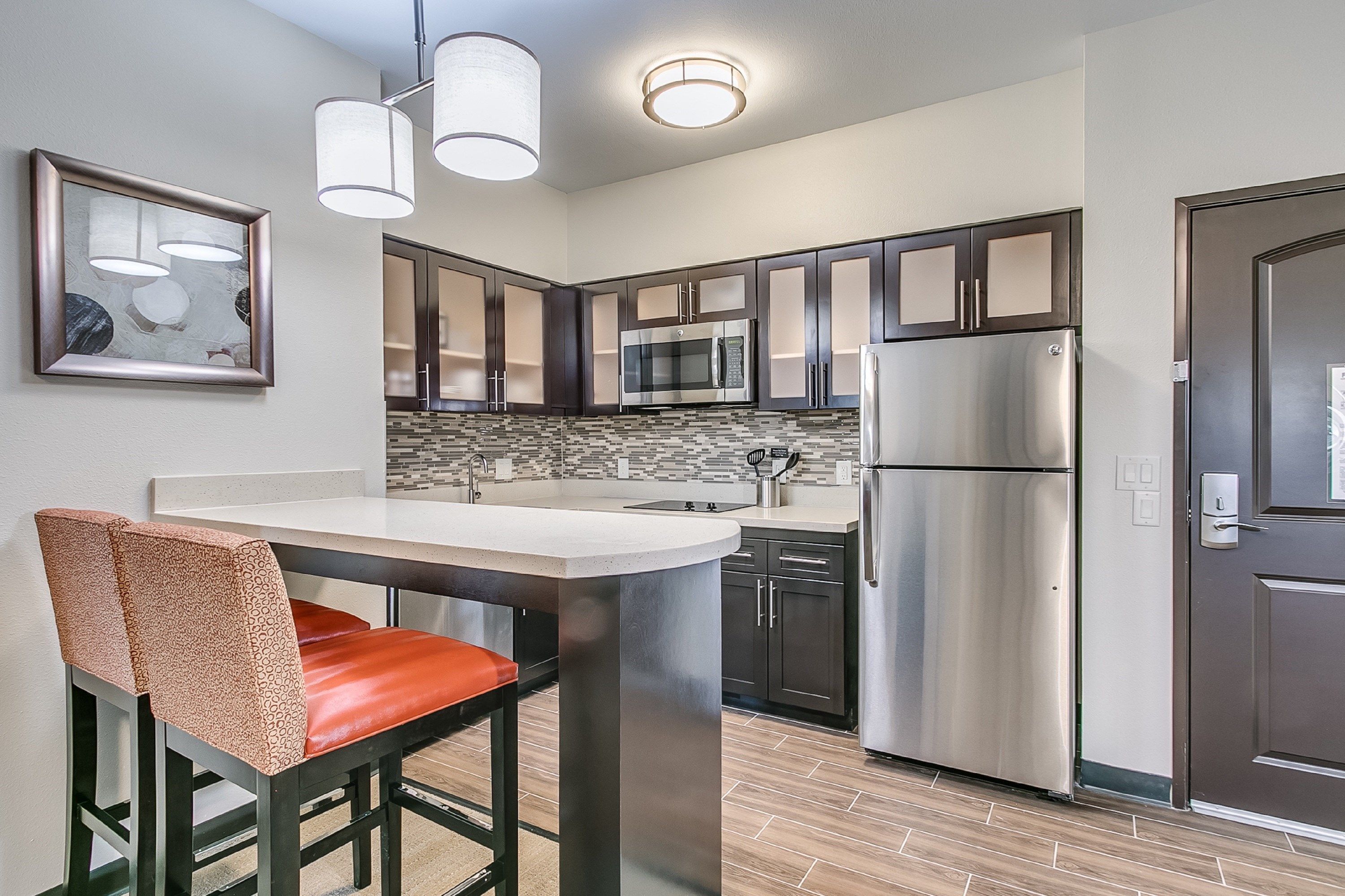 A modern kitchen with stainless steel appliances, a central island, and a dining area with a chair.
