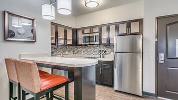 A modern kitchen with stainless steel appliances, a central island, and a dining area with a chair.