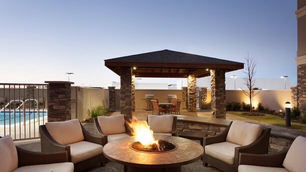 A patio area with a fire pit, wicker furniture, and a pool in the background.