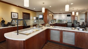 A hotel breakfast area with a buffet setup, including a self-service station with various food items and a coffee station.