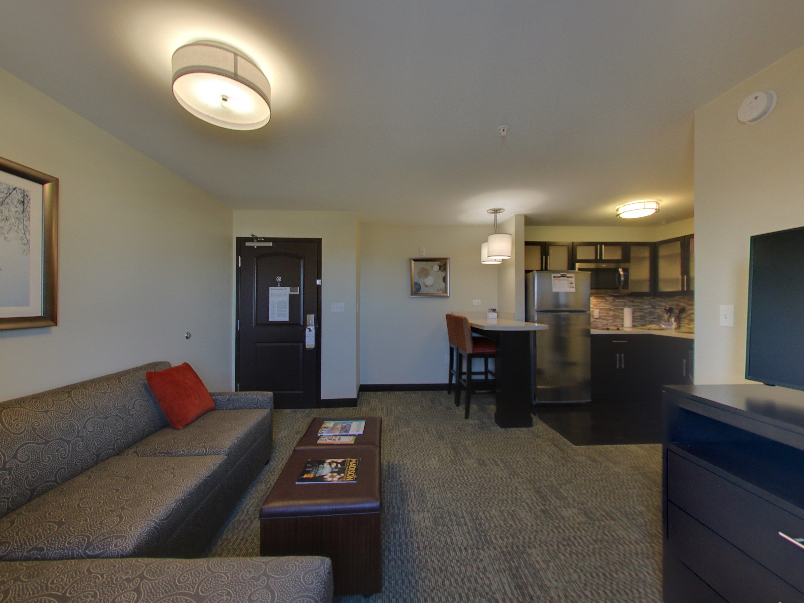 A hotel room with a sofa, a small table, a kitchenette, and a TV.
