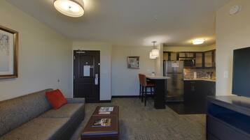 A hotel room with a sofa, a small table, a kitchenette, and a TV.