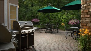 Eine Außenpatio mit Grill, Tischen, Stühlen und Sonnenschirmen.