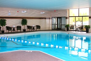 An indoor swimming pool with clear lane dividers, a tiled floor, and several chairs and tables around the pool area.