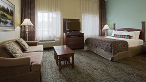 A hotel room with a bed, a sofa, a television, and a small table. - Studio Suite in Tallahassee | FREE Breakfast + On-Site Business Center (Tallahassee)