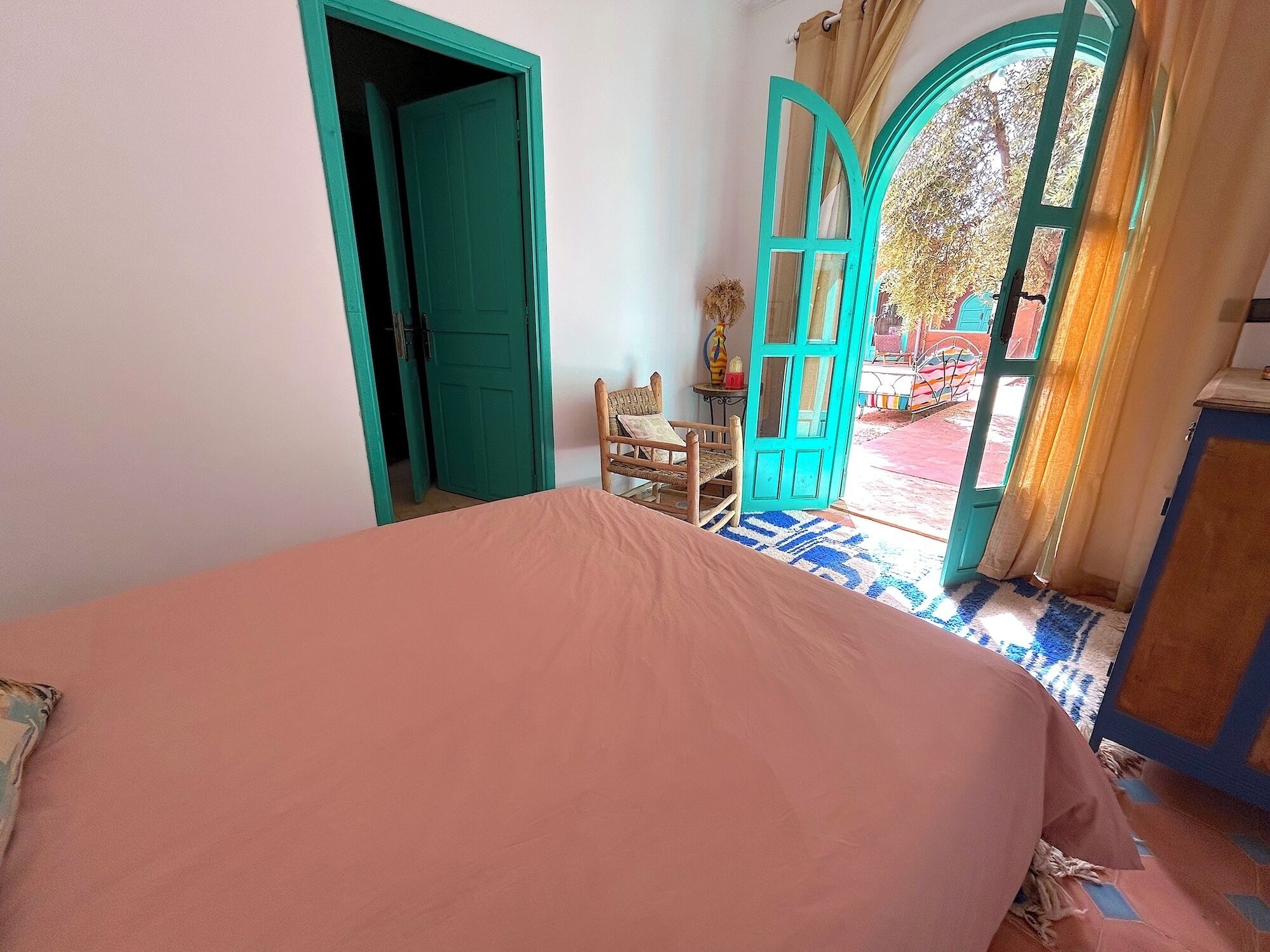Un dormitorio con una cama, una silla y dos puertas abiertas que dan al exterior.