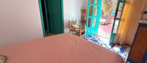 Un dormitorio con una cama, una silla y dos puertas abiertas que dan al exterior.