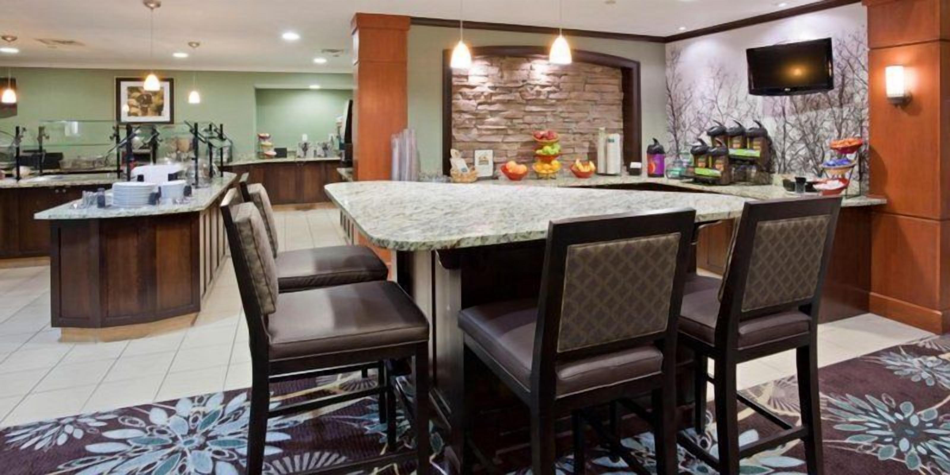 Comedor de hotel con mostrador de mármol, sillas de madera, pared decorativa de piedra y televisor de pantalla plana.