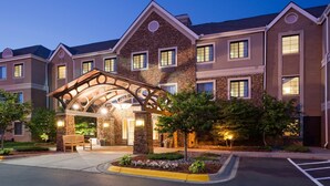 A multi-story hotel with a stone facade, a covered entrance, and a landscaped front yard. - Cozy Studio | Free Breakfast. Pool & Gym. (Maple Grove)
