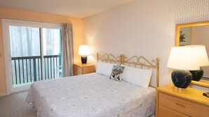 Une chambre à coucher avec un grand lit, une table de chevet, une commode, une fenêtre avec des rideaux et un mur recouvert d’un papier peint à motifs.
