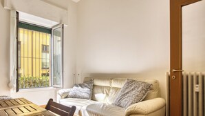 A room with a beige sofa, a wooden table, a window with a view of a yellow building, and a radiator. - Adorable flat near centre (Milan)