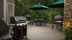 An outdoor patio with a grill, tables, chairs, and umbrellas.