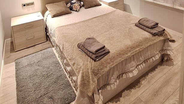 A bedroom with a large bed, two bedside tables, a nightstand, a rug, and a window with curtains. - Fantastic house in a quiet area. (Salitja)