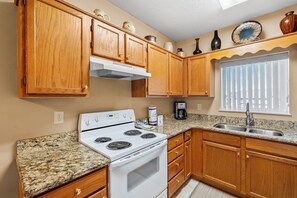 A kitchen with wooden cabinets, a white stove, granite countertops, and a window with blinds.