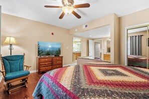 A bedroom with a large bed, a ceiling fan, a wooden chair, a dresser, and a painting on the wall.