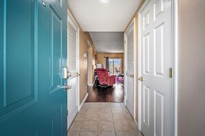 A hallway with teal and white doors, a red chair, and a view of a room with a window.