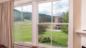 A room with a large window offering a view of a green landscape and a red building across the street. - Okemo | Studio Condo + Close to All Amenities (Ludlow)
