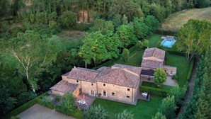 A stone building with a tiled roof, surrounded by lush greenery and a swimming pool. - L'orto Vignamaggio Private Pool Nature (Greve in Chianti)