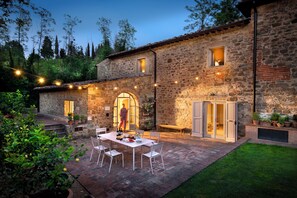 Un bâtiment en pierre doté d’un patio, d’un espace extérieur aménagé avec des sièges et de guirlandes lumineuses.