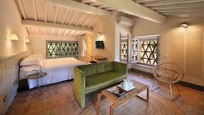 A room with a bed, a green sofa, a wooden coffee table, a wicker chair, and a window with a geometric pattern. - L'orto Vignamaggio Private Pool Nature (Greve in Chianti)