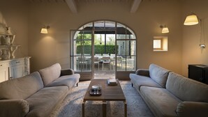 A spacious living room with two sofas, a coffee table, and a large arched window providing a view of the outdoors. - L'orto Vignamaggio Private Pool Nature (Greve in Chianti)