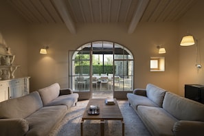 Relax in a spacious living area with a high ceiling and large window overlooking a patio.