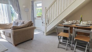 Ein gemütliches Wohnzimmer mit einer Couch und einem Esstisch für vier Personen. Eine Treppe führt zu einer oberen Ebene.
