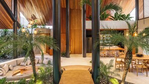Un área de piscina interior moderna con suelo de madera que conduce a un espacio de descanso, rodeada de plantas tropicales y un comedor.