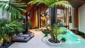 Un área de piscina moderna al aire libre con techo de madera, rodeada de plantas y un espacio para sentarse.