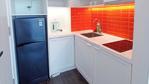 A compact kitchen with white cabinets, a black refrigerator, a red-tiled backsplash, and a sink.