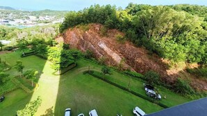 A high vantage point view of a landscaped area with a grassy lawn, a few parked cars, and a steep, rocky hillside.