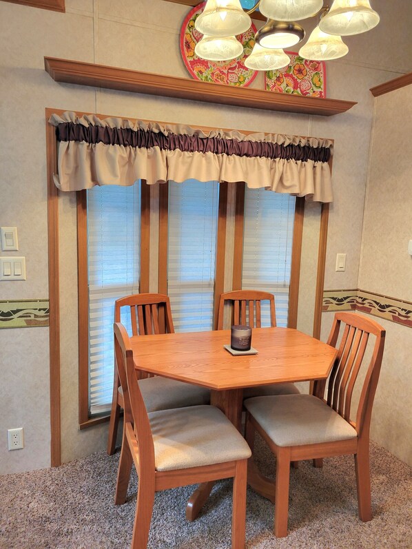 A dining area with a wooden table and four chairs, a decorative window valance, and a ceiling light fixture.