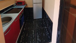 A compact kitchen with a refrigerator, microwave, and red cabinets. - Appartement meublé GOLF (Bamako)