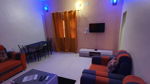 A living room with a sofa, a coffee table, a TV, and a ceiling fan. - Appartement meublé GOLF (Bamako)