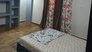 A bedroom with a bed, a ceiling fan, a wardrobe, and a curtain with a floral pattern. - Appartement meublé GOLF (Bamako)