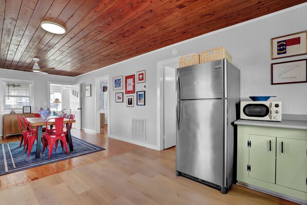 A modern kitchen with a stainless steel refrigerator, a microwave, and a green cabinet. There is a dining area with red chairs and a blue rug.