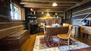 A rustic cabin interior with a wooden dining table, chairs, a refrigerator, and a coffee machine. - Historic Sadie's Log Cabin (McGregor)