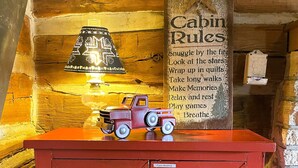 A red cabinet with a toy truck on top, a wooden wall with a hanging sign, and a lamp. - Historic Sadie's Log Cabin (McGregor)