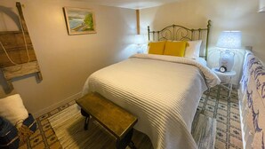 A neatly made bed with a headboard, a bedside lamp, and a small table beside it. - Cozy Alpine Retreat in Historic Downtown (McGregor)